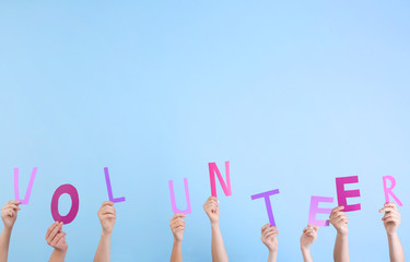 Canvas Print - People putting hands in air together with word made of paper letters on light background. Volunteering concept