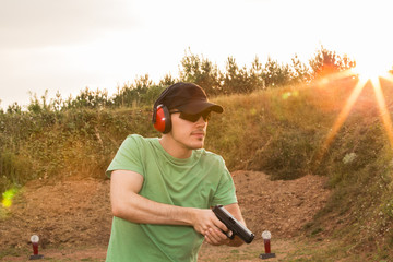 Caucasian military soldier or special force unit or policeman training on the field with the pistol ready to kill the enemy target criminal with gun  pistol in his hands. Sunset in the nature