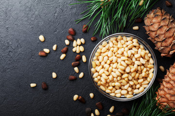 Wall Mural - Heap of pine nuts and cedar cones on black table top view. Organic and healthy superfood.