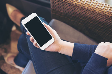 mockup image of a woman's hand holding white mobile phone with blank black screen on thigh sitting o