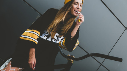 Wall Mural - Outdoor lifestyle portrait of pretty sexy lookin young girl in hockey jersey style dress posing on gray wall background with street bicycle