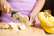 Woman slice ripe banana on wooden board for cooking or processing in the kitchen