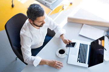 Wall Mural - Businessman with smartphone and laptop in his office.