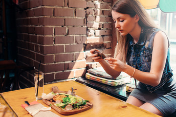 Young woman wearing casual clothes taking picture of her healthy lunch sitting on windowsill in trendy cafe