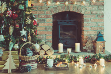 Wall Mural - Beautiful Christmas setting, decorated fireplace with woodburner, lit up Christmas tree with baubles and ornaments, lantern, stars and garlands, selective focus