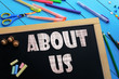 © mizinra - The text About us on a black chalkboard on the table with school accessories (pens, pencils, brushes)