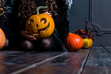 girl sitting near the Halloween pumpkin head jack lantern on dark wooden background, concept of a holiday Halloween