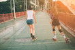 Two slim and sexy young women and roller skates. One female has an inline skates and the other has a quad skates. Girls ride in the rays of the sun