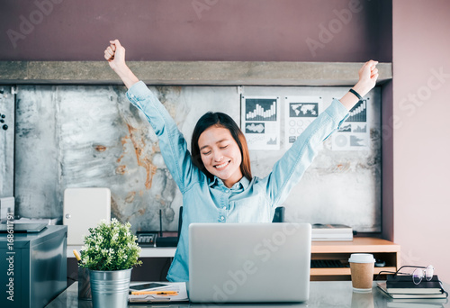 Plakat Azjatycki projektant kreatywny podnieść rękę i zamknąć oko przed laptopa na biurku, zrelaksować się od ciężkiej pracy w biurze