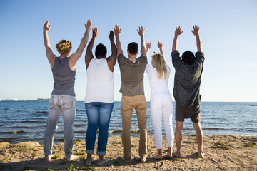 Rear view of ecstatic teens standing on sandy beach in front of water