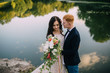© MZaitsev - Happy newlyweds standing and smiling on the river bank