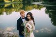 © MZaitsev - Happy newlyweds standing and smiling on the river bank