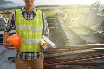 Wall Mural - Engineer or Safety officer holding hard hat with blueprint on building construction site