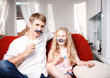 © Maksim Kostenko - Joyful father and daughter with artificial mustache while sitting togheter on red chair at home.