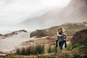 Wall Mural - Man giving woman piggyback on winter beach