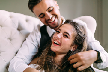  A young couple in love having fun on a sofa and playing with a hair of the girl. Cheerful bride and groom laughing, close-up. Soft focus on the girl