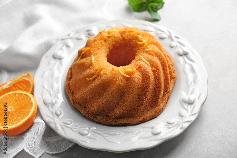 Plate with delicious citrus cake and orange zest on light table