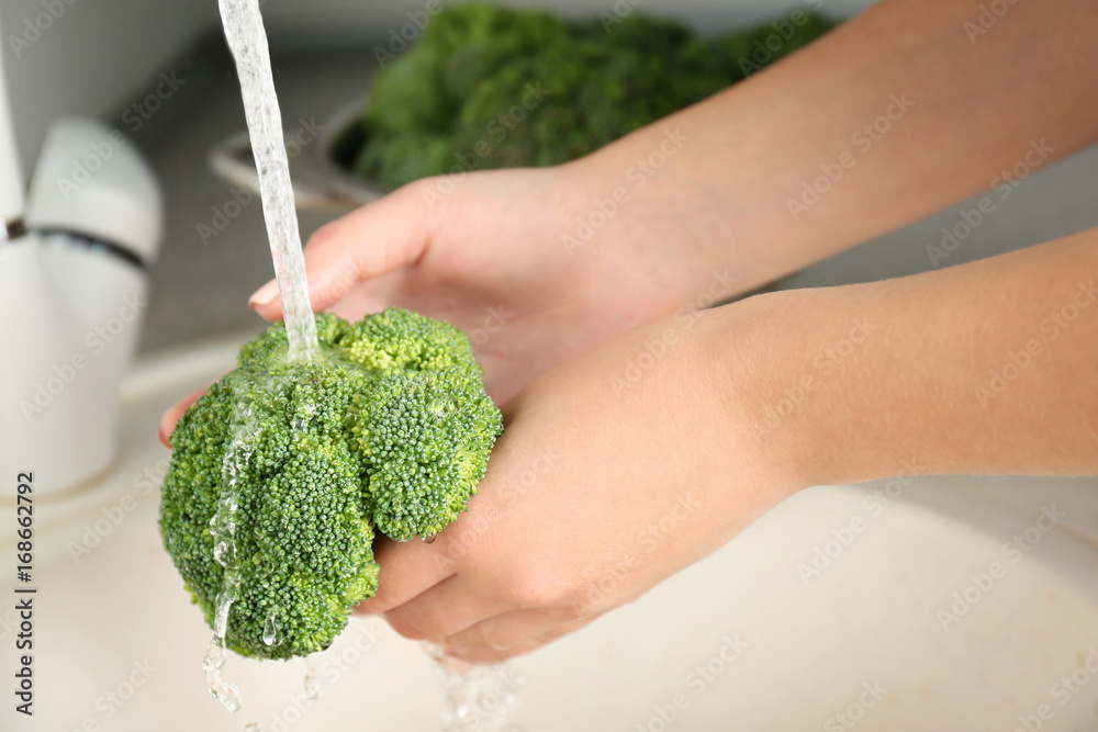 Woman's hands holding broccoli sprouts under running water in kitchen sink