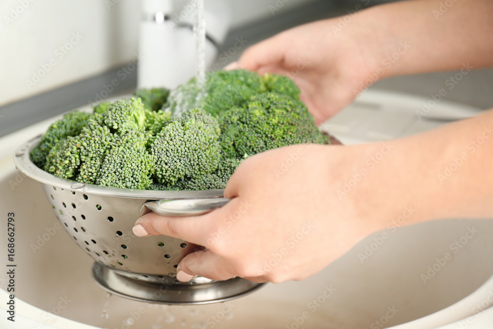 Woman's hands holding broccoli sprouts under running water in kitchen sink