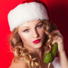  beautiful young woman wearing Santa Claus costume holding green old phone receiver against red background