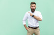 Wow! Handsome young adult man with beard in shoked. Pointing away while standing isolated on light green background