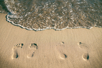 Footsteps on a sandy beach. Wave and sun. Holiday and travel concept. Summer vibes.