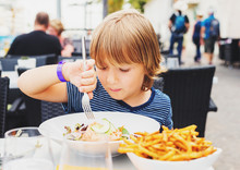 Little Boy Having Lunch In The Restaurant, Child Eating Fresh Salmon Salad And French Fries