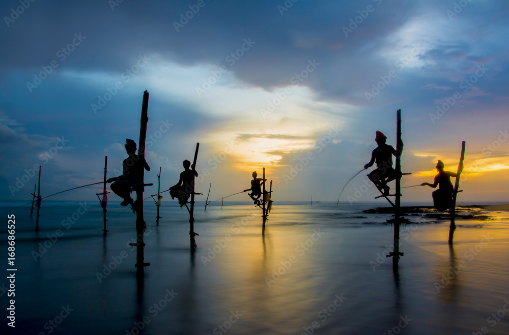 Silhouettes of the traditional Sri Lankan stilt fishermen on a stormy in Koggala, Sri Lanka. Stilt fishing is a method of fishing unique to the island country of Sri Lanka - obrazy, fototapety, plakaty 