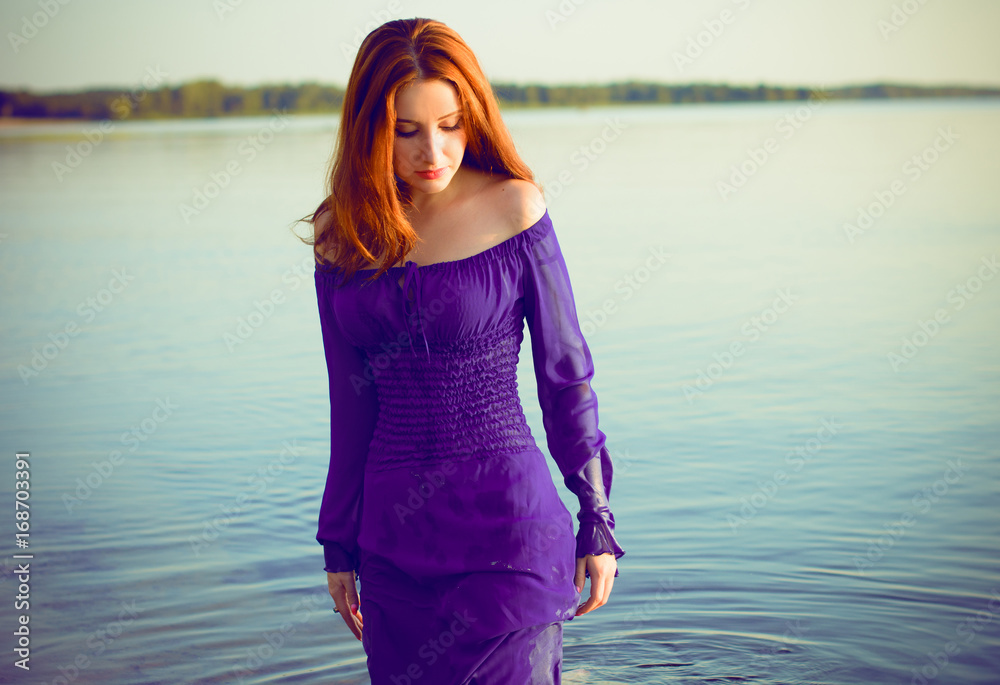 Photo Stock Gorgeous hot young red haired lady at evening sunlight around  forest, rocks and water. Woman wearing in purple long dress. Portrait in  vintage style.Sweet woman rest on the sea.Nymph on