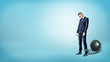© gearstd - A depressed businessman on blue background stands with a lowered head while chained to an iron ball.