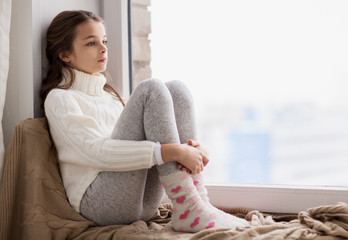 Wall Mural - sad girl sitting on sill at home window in winter