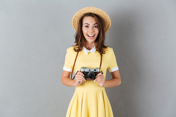 Cheerful young girl in hat holding retro camera