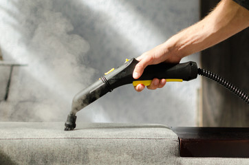 Hand cleaning a  sofa with a steam cleaner. Home cleaning concept.