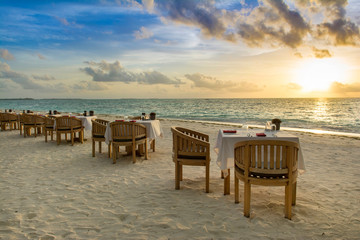 Tropical restaurant on the sandy beach. Landscape of beautiful sunset in Maldives island with colorful sky and dramatic clouds over wavy sea.