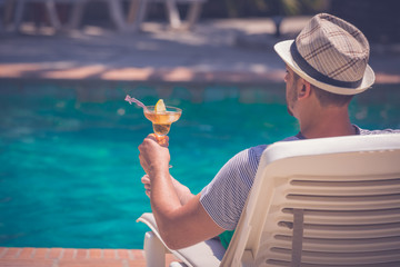 Man relaxing next to the swimming pool and holding copacabana cocktail