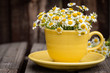 Yellow cup filled with chamomile flowers on wooden plank table.