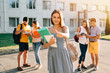 © Maksym Azovtsev - Happy beautiful girl standing with note books and backpack showing thumb up and smiling, standing near university building, her friends are behind