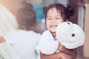 Wall Mural - Happy asian child girl smiling and hugging her doll with love in the house in vintage color tone