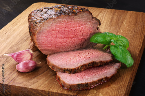 Obraz na plátně Baked meat, garlic and basil on a wooden background. Roast beef.