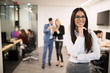 © NDABCREATIVITY - Businesswoman posing while other businesspeople talking in background
