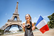 Young and happy woman tourist with french flag and photo camera in front of the Eiffel tower in Paris