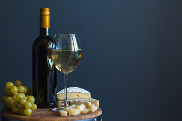 Bottle and glass with white wine near cheese composition on a wooden board