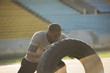 An athletic black man is performing tractor tire exercizes, flipping it