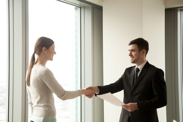 Wall Mural - Happy businessman and businesswoman shaking hands while standing in office, satisfied partners reach agreement after effective successful negotiations, making sealing good deal, concluding contract