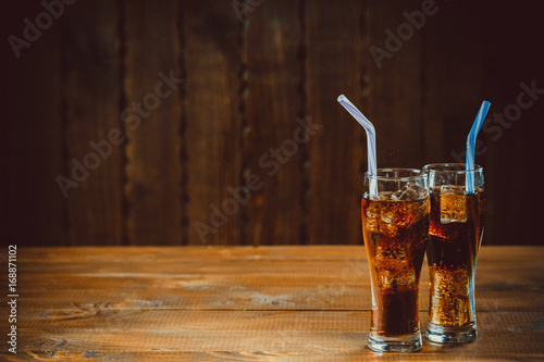Fotografia Beautiful cold drink of Cola with ice cubes with a boiler straws in glasses on wooden background with free space