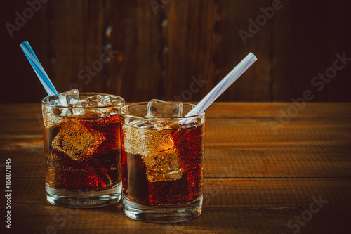 Fotografia Beautiful cold drink of Cola with ice cubes with a boiler straws in glasses on wooden background with free space