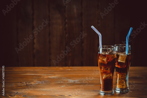 Stampa su Tela Beautiful cold drink of Cola with ice cubes with a boiler straws in glasses on wooden background with free space