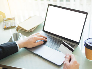 Close-up of hands shopping and paying online using white screen laptop and credit card