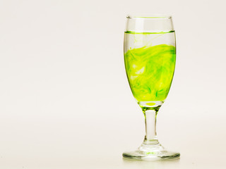 Green food coloring diffuse in water inside wine glass with empty copyspace area for slogan or advertising text message, over isolated grey background.