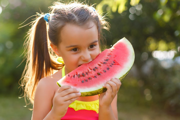 Wall Mural - Child eating watermelon in the garden. Little girl holding a slice of watermelon and smiling.